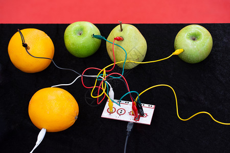 水果电池与设备以及显示的苹果橙子和梨连接的电缆背景