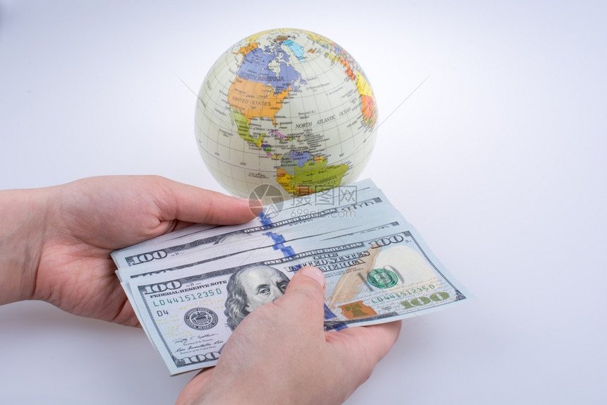 人类手拿着美元钞票站在一个白色背景的模范地球旁边图片