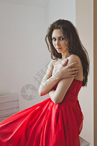 穿着长红色晚礼服的女孩肖像穿着正式礼服的女孩站在窗边6021背景图片