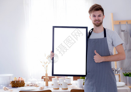 英俊的厨师在餐厅菜单或食谱上显示空白的菜单牌或带有厨房背景的食谱图片