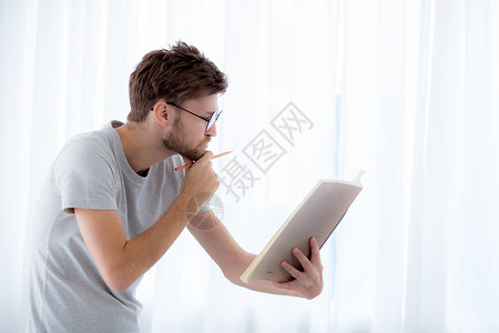 戴眼镜的帅哥正在读书准备考试和思站在起居室教育概念背景图片