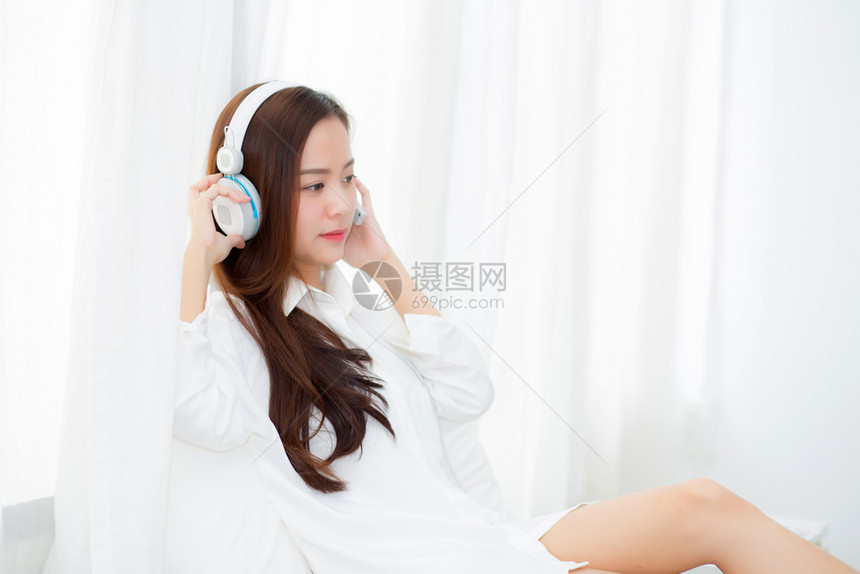 美丽的年轻女坐在卧室时享受耳机听音乐图片