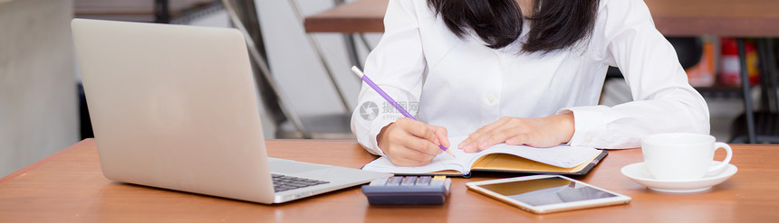 女在笔记本上写用电脑女孩在咖啡店工作自由职业的概念图片