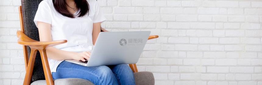 网路上美丽的亚洲年轻女在网上笔记本电脑工作坐在水泥砖白色背景的椅子上女孩使用笔记本电脑商业概念图片