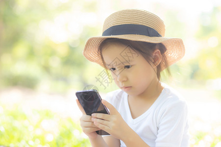 在花园里使用智能手机微笑的美丽亚洲孩子在公园的互联网络上玩游戏时图片