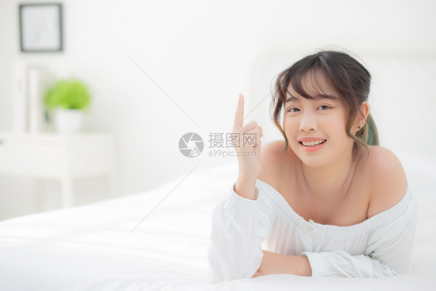 美貌丽的年轻女早上微笑起来健康美貌女孩躺在床上指着一些皮肤护理和化妆品装饰着快乐生活方式和放松的概念图片