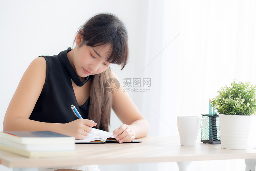 美丽的年轻女士在家中客厅里微笑地坐着学习写笔记本和日做女孩功课在桌子上工作的商业妇女教育概念图片