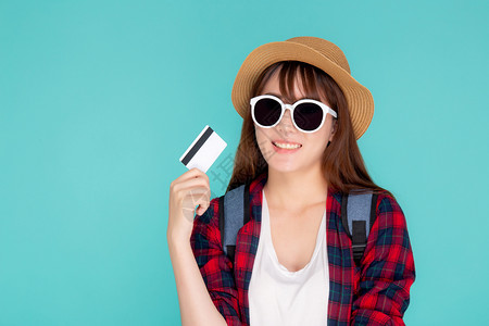 美丽的年轻女士戴着帽子和墨镜拿着信用卡前往蓝背景的夏日旅行假期高清图片素材