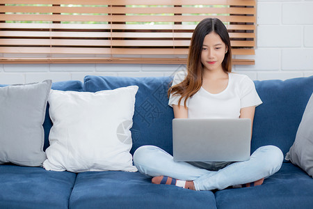 年轻的亚洲女商人微笑在家工作时使用笔记本电脑连线在客厅沙发上网自由职业女孩在沙发上使用笔记本背景图片