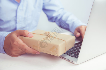 手持Kraft纸赠品盒手持笔记本电脑在木制桌子上线购物供圣诞节或周年纪念礼物季节和在社会动荡期间庆祝背景图片