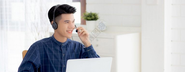 从事膝上型计算机工作在家戴耳机的年轻亚洲商人身戴头盔的商人负责电视会议通信和教育男学习和电子互联网高清图片素材