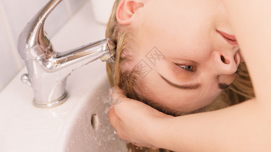洗头发的女人在浴室水槽里洗长金发在家理的概念洗头女人在浴室水槽里洗头发背景图片