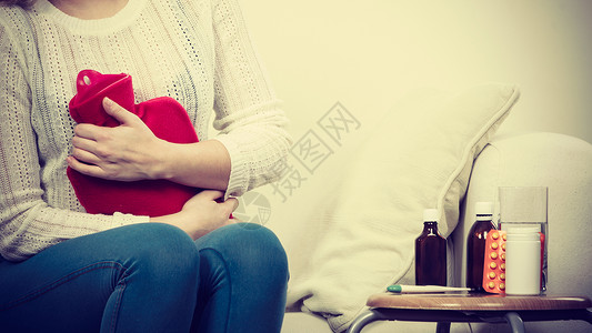 月经来了胃痛期和月经抽筋问题概念在可口上坐着肚子抽筋的妇女感觉非常不舒服用热水瓶来感到宽慰在可口乐上坐着肚子抽筋背景