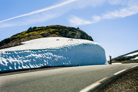 挪威Aurlandsfjellet山道高雪墙上拍摄照片的旅游女客背景图片