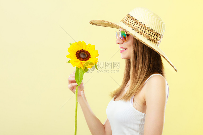 更近的一面观察着穿墨镜的迷人夏天女穿着墨镜的草帽手上拿着向日葵背黄色景的向日葵图片