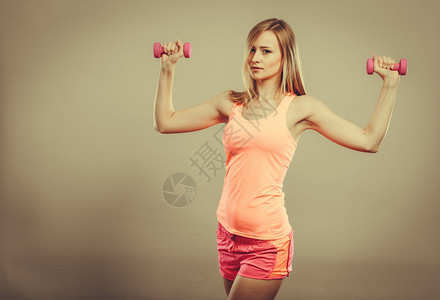 健壮体强的女人与哑铃一起锻炼肌肉健壮的金发女孩举重制片厂拍摄图片