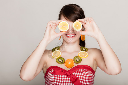 有新鲜柑橘水果项链的女孩眼睛遮着柠檬在灰色上玩得开心女人建议健康食物图片
