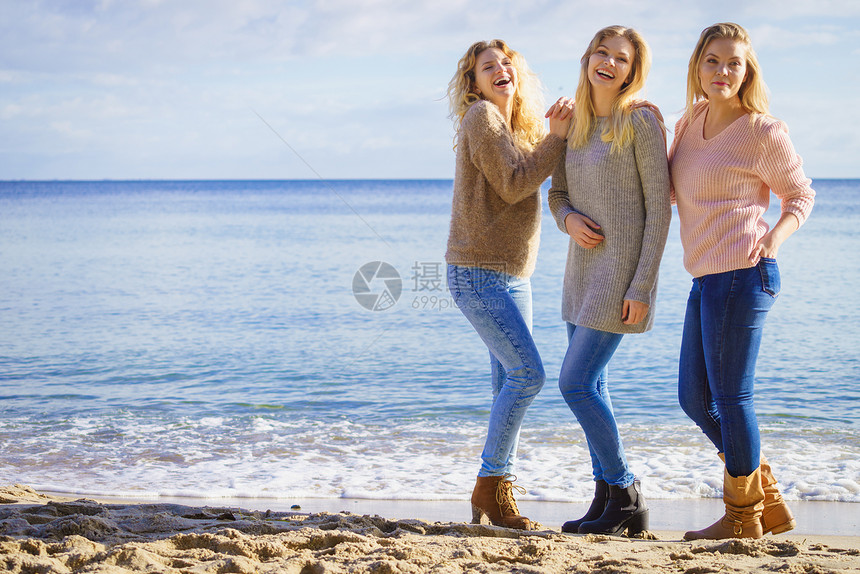 在温暖的秋天气下三名穿着毛衣的时尚女在阳光明媚的海滩上闲时间度过图片