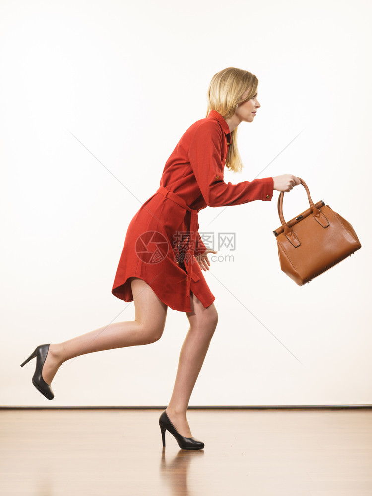时装的漂亮年轻女子穿着优雅的红色短的裙手持皮包匆忙跑的皮包图片