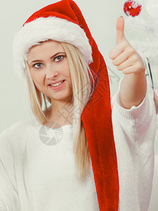身戴圣诞老人红帽子的快乐年轻女想到圣诞礼物和节假日举起拇指的手势图片