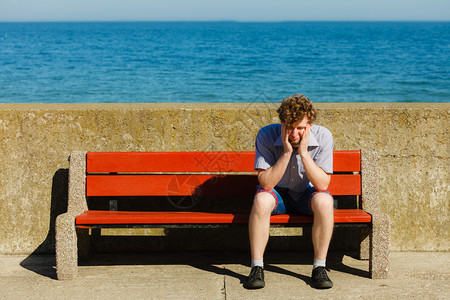 疲惫不堪的人坐在海边长椅上年轻人在户外放松暑假疲倦的人坐在海边长凳上图片