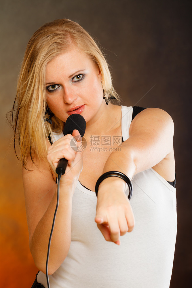 卡拉OK音乐歌手概念金发女人的肖像唱给麦克风年轻明星表演玩得开心摄影棚拍金发女人唱给麦克风图片