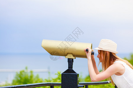 穿戴太阳帽子的女游客透过望远镜向处看图片