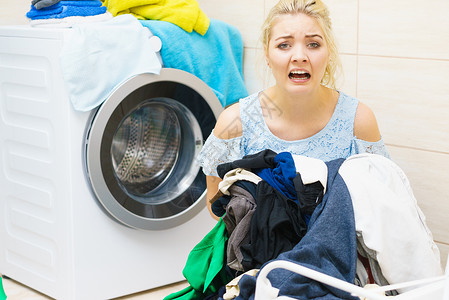 身处一堆大衣物的不幸女坐在洗衣机旁边做着疲劳的家务女性的高清图片素材