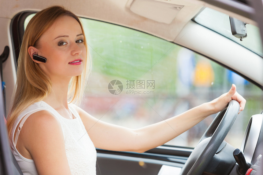 年轻金发女青年用手机和头盔驾驶汽车侧视妇女用耳机驾驶汽车图片