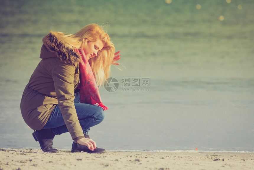 妇女穿着温暖的夹克在海边滩上放松阳光寒冷的一天图片
