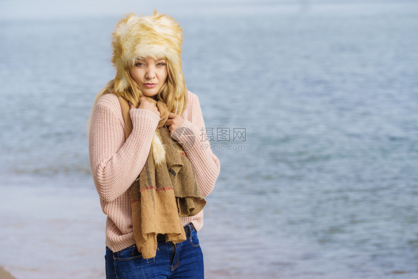 穿着温暖时髦的秋天服装盛着毛大帽子但感到寒冷的女子在海滩散步时感到寒冷的女子穿着时髦服装的女子在海上感到寒冷图片