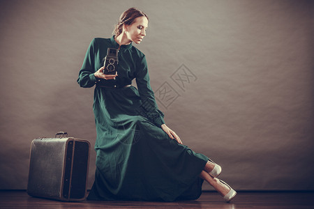 妇女古老风格长的深绿色袍老旧手提箱和相机拍照旧片背景图片