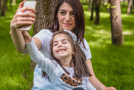 年轻妈和小女孩一起玩自拍母亲和女儿充满爱自然情感的快乐时刻年轻母亲和女儿在绿草上玩得很开心背景图片