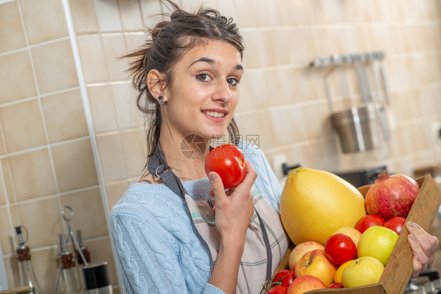 在厨房里有各种水果的年轻笑容女子图片