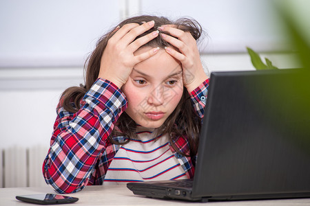 一个无聊的少女正在用笔记本电脑做家庭作业背景图片