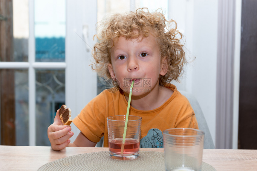 一个可爱的小男孩喝红果汁用稻草图片