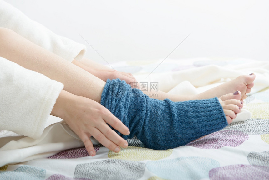 美丽的年轻女把羊毛蓝袜子放在床上图片