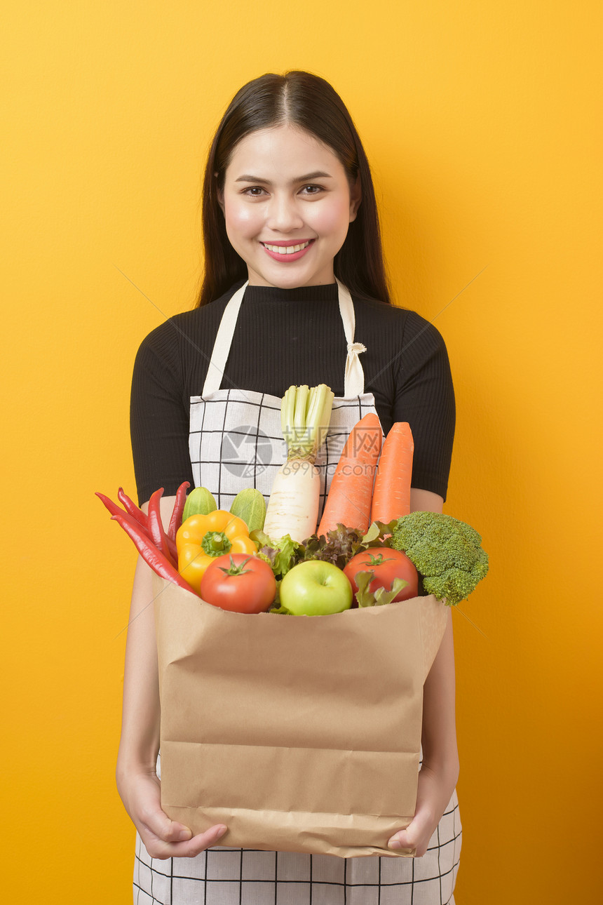 美丽的年轻女士拿着蔬菜在杂货袋黄色背景工作室黄色背景图片