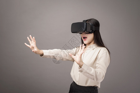 美丽的女人在灰色背景上使用虚拟现实图片