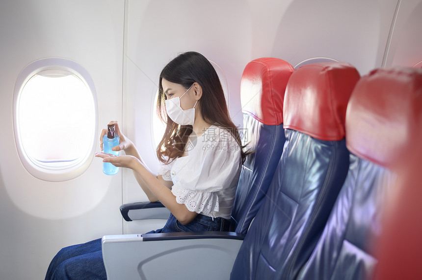 乘客坐在机舱内佩戴着口罩用酒精给手消毒图片