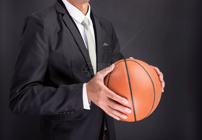 青年商人持有以黑色背景孤立的篮球图片