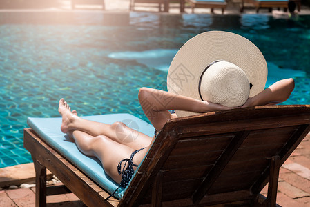 戴大帽子的亚洲女青年在游泳池边的蓝水中晒日光浴背景图片
