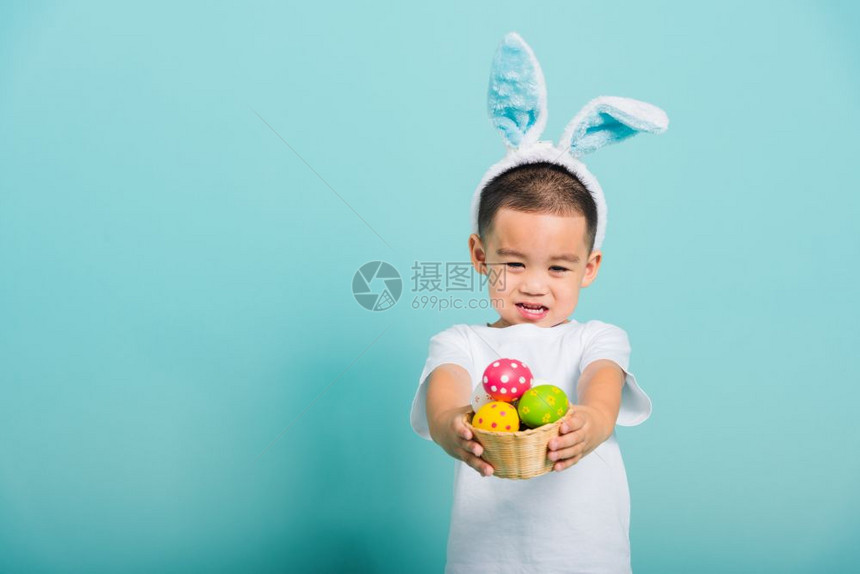 亚洲可爱的小孩男微笑带着兔子耳朵和白色T恤衫站在篮子上着图片