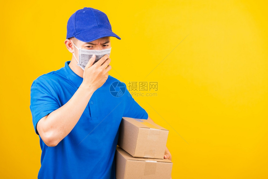 身穿蓝色T恤衫和帽子制服的亚洲年轻送货工人身穿蓝色T恤衫和帽子制服的亚洲年轻送货员身着面罩在服务客户使用科罗纳或COVID19服图片