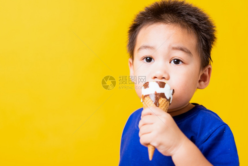 快乐的亚洲儿童或孩子可爱的小男孩快乐肖像亚洲儿童或孩子可爱的小男孩有吸引力的笑玩着吃甜巧克力冰淇淋华芙饼摄影棚拍孤立在黄色背景上图片