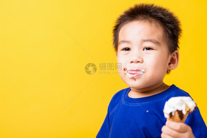 快乐的亚洲儿童或孩子可爱的小男孩快乐肖像亚洲儿童或孩子可爱的小男孩有吸引力的笑玩着吃甜巧克力冰淇淋华芙饼摄影棚拍孤立在黄色背景上图片