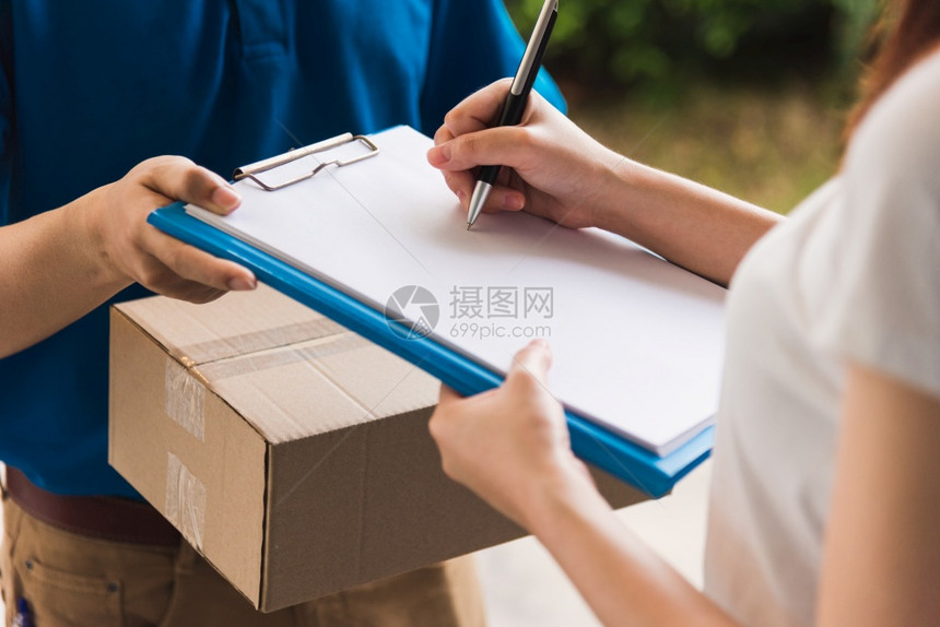 亚洲青年送货员在网上与包装邮箱一起购买亚洲青年送货员的包裹式邮箱装在统一的保护面罩冠状中他利用家庭纸本上的笔签COVID19向服图片