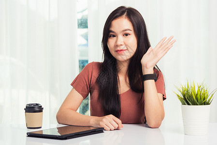 在家工作亚洲商界年轻美丽的女士坐在办公桌工作空间上微笑手举向您问好与团队视频聊天或家庭办公室数字平板电脑会议男人高清图片素材