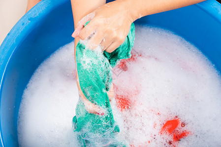 蓝色泡沫近身的亚洲年轻女子在盆地用手洗彩色衣服带涤剂有肥皂泡水工作室拍摄背景洗衣服概念背景