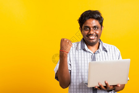 年轻黑人兴奋地握着笔记本电脑紧拳头并举起手来为胜利者举庆祝他的成功图片